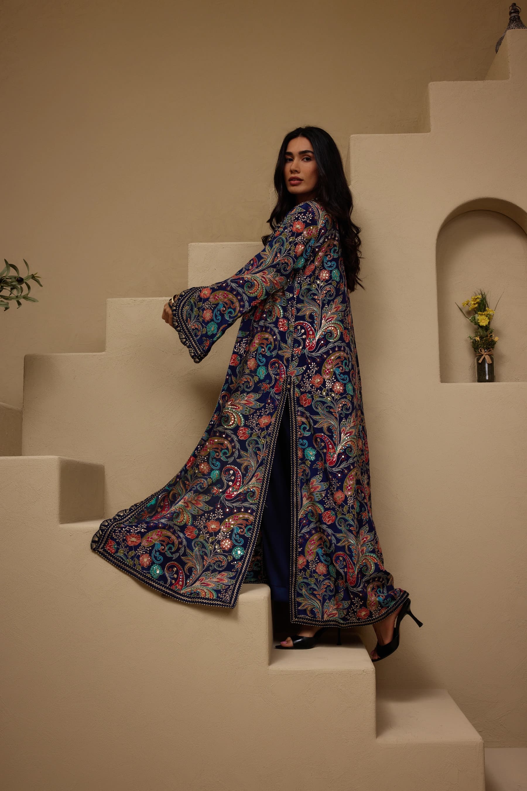 Model in a navy paisley-embroidered open abaya walking up plaster steps in the Sand room