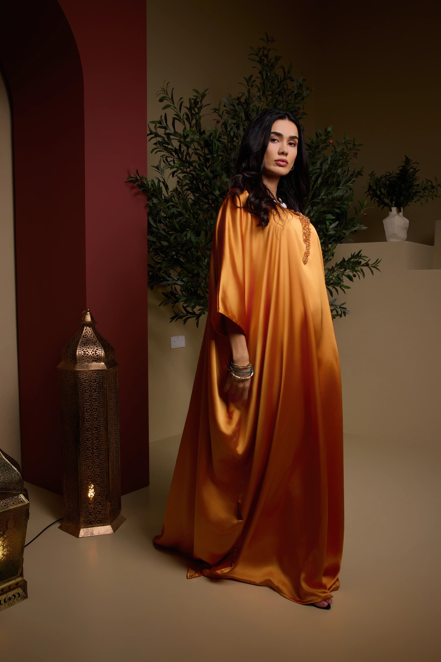 Model in a flowing saffron satin kaftan beside a brass floor lantern in the Heritage room