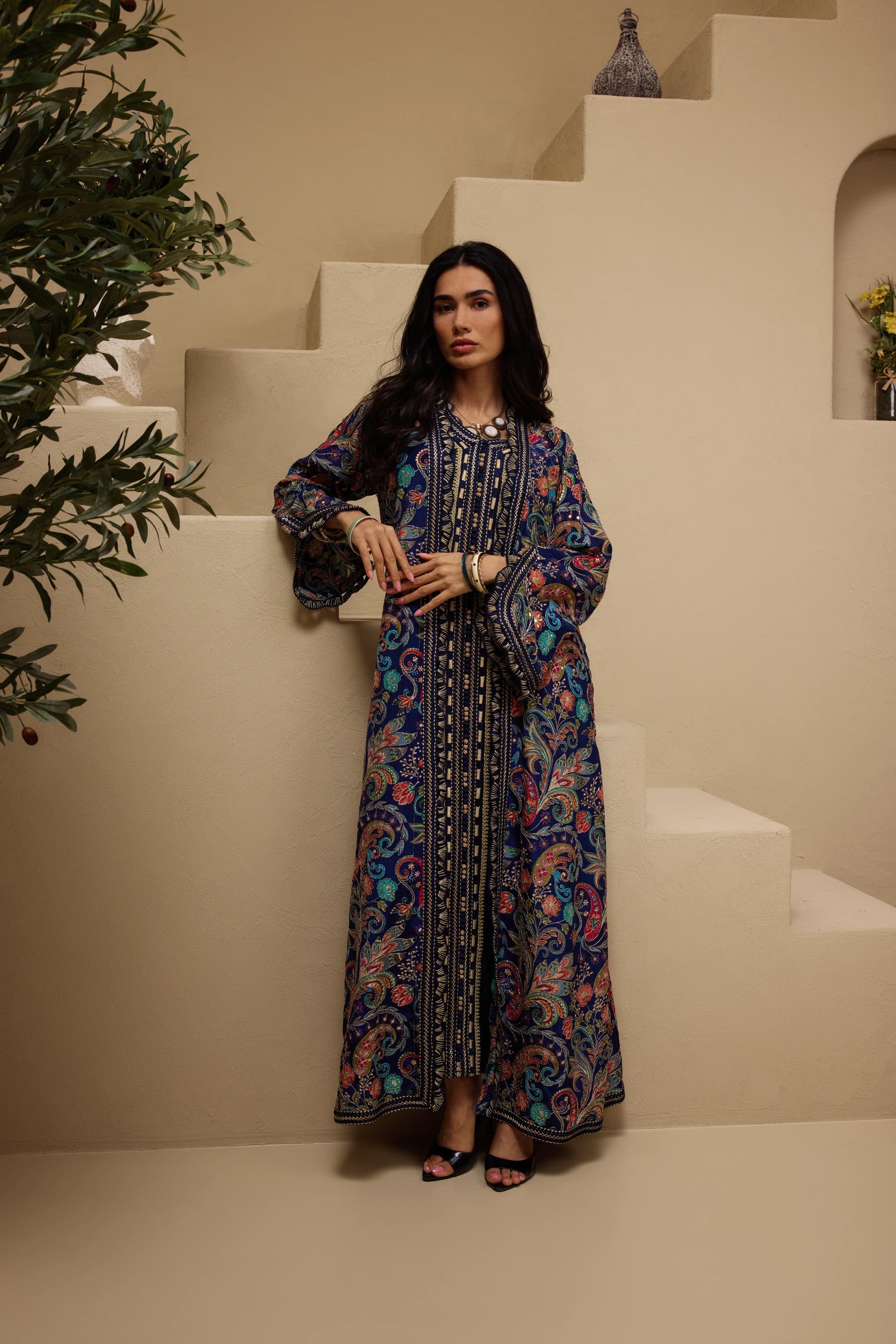 Model in a navy paisley abaya with flared sleeves, standing in front of the plaster steps of the Sand room
